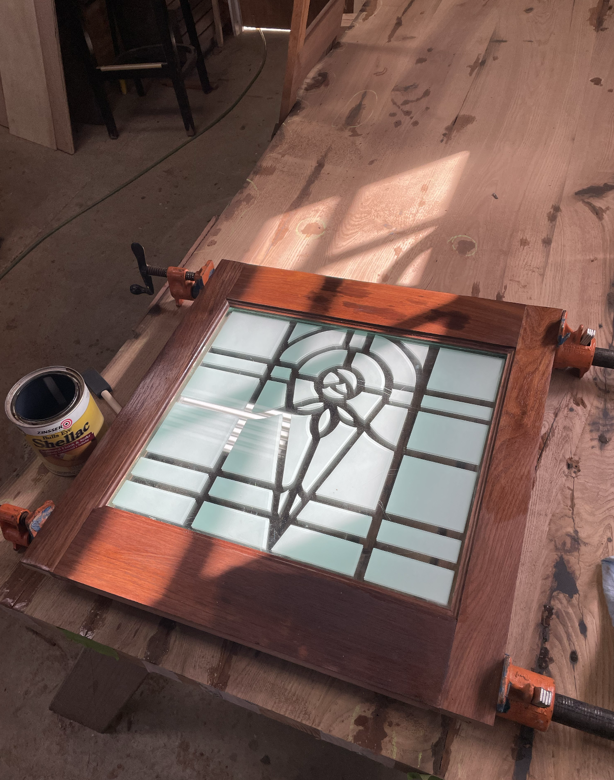 Custom mahogany cabinet door clamped on the bench, fitted with original leaded-glass panel featuring a stylized rose motif, finished in shellac