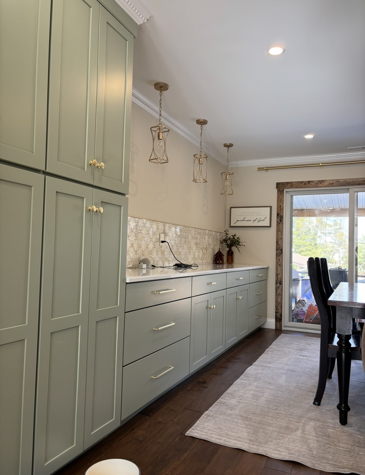 Sage shaker pantry and base cabinets with brass pulls and pendant lights