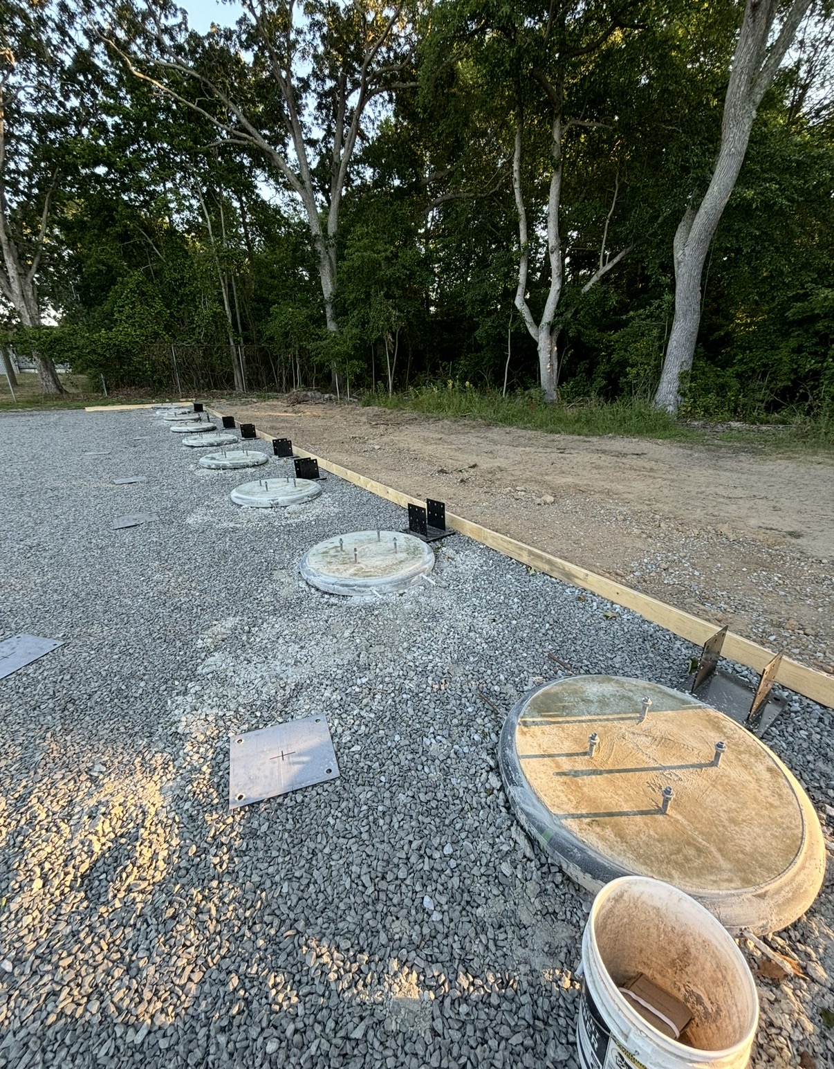 Concrete pier footings set on a gravel pad with anchor bolts and bracket plates ready for posts